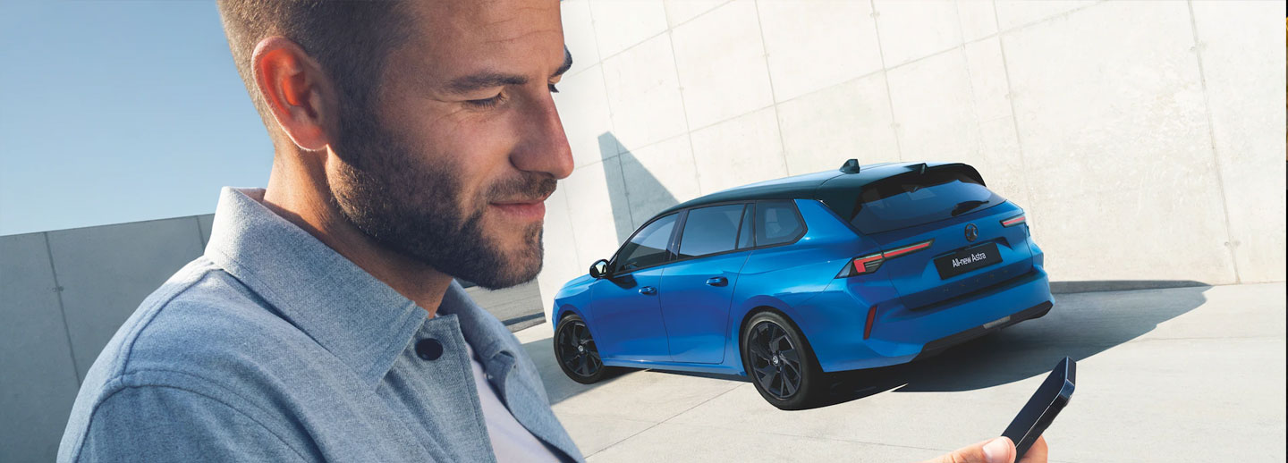 Man standing with phone by Vauxhall Astra in Cobalt Blue
