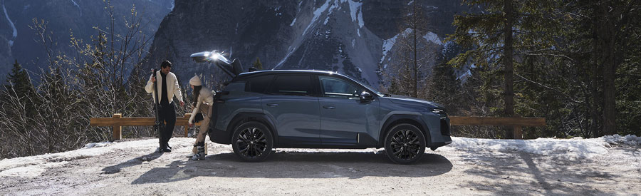 Couple stood behind a Citroen C5 Aircross in Astoria Green with Mountains in the background.