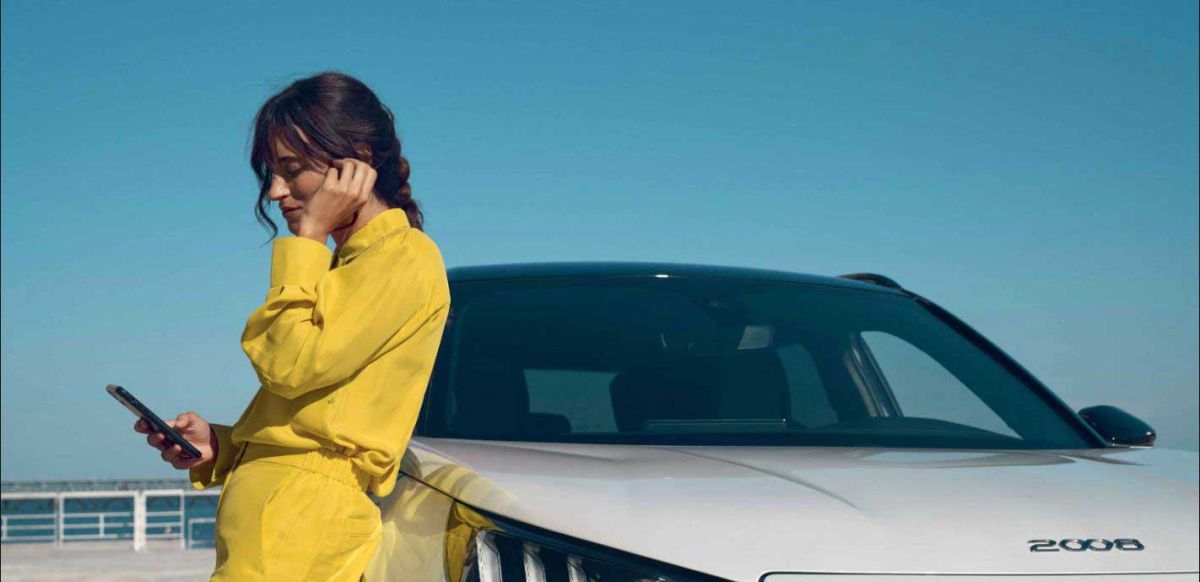 A lady is leaning on a white Peugeot 2008 while on her phone