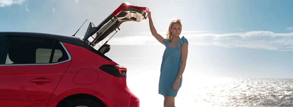 Lady on a beach, standing to the rear of a Vauxhall Corsa with boot open