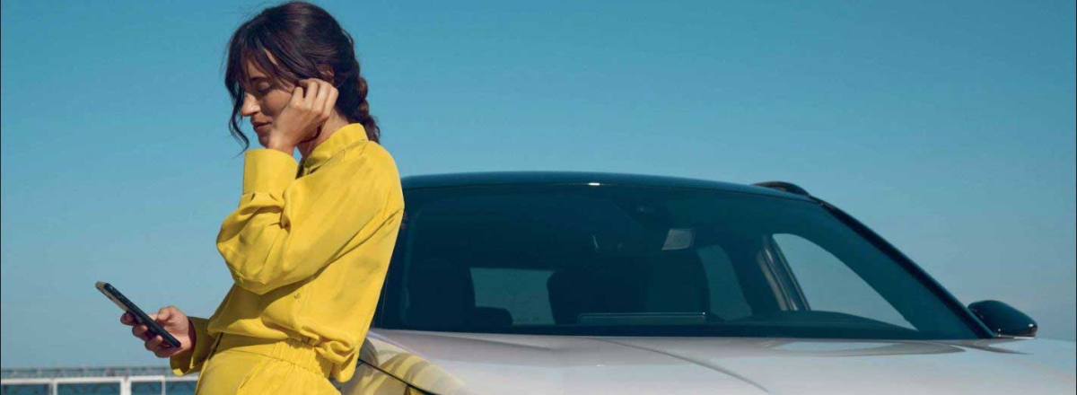 A lady is leaning on a white Peugeot 2008 while on her phone