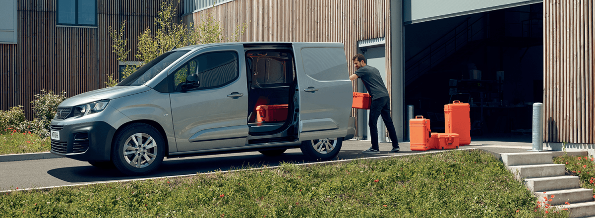 Man wearing a grey shirt loading a silver Peugeot Expert with orange tool boxes.