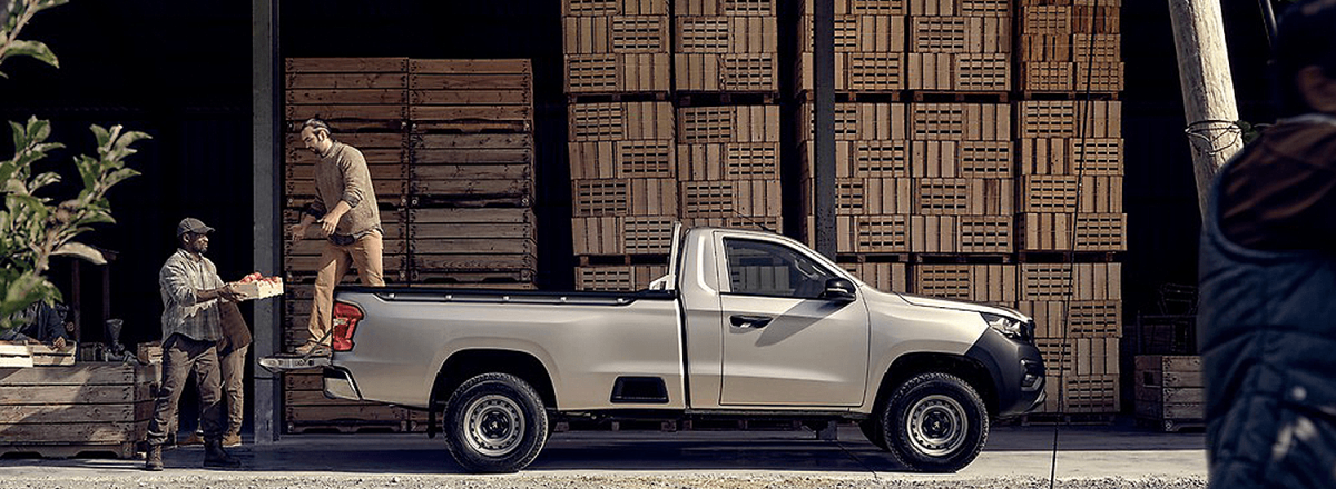 Side view of a man loading cargo into the bed of a Peugeot Landtrek.