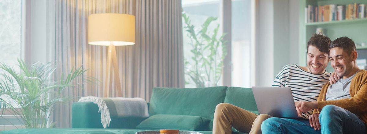 Couple looking at a laptop screen together while sat on a green sofa.