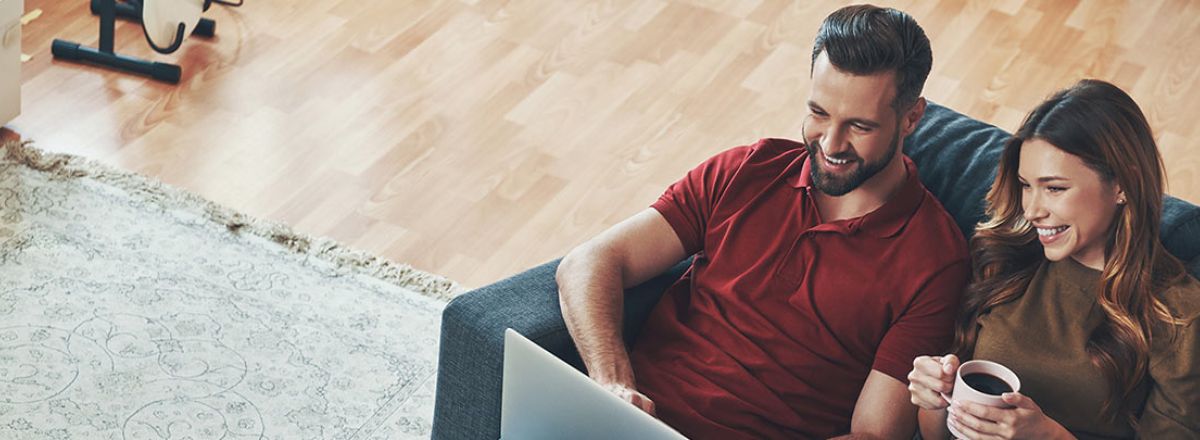 A lady and man sat on a sofa looking at a laptop.