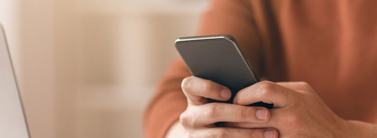 A man in an orange jumper using his phone to switch to paperless.