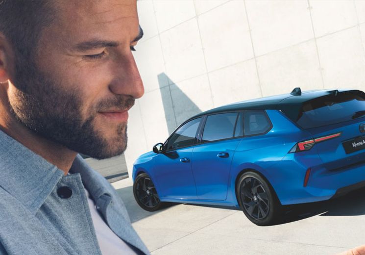 Man standing with phone by Vauxhall Astra in Cobalt Blue