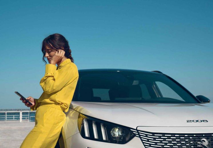 A lady is leaning on a white Peugeot 2008 while on her phone