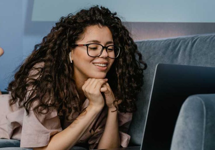 Smiling lady laying on the sofa on her laptop