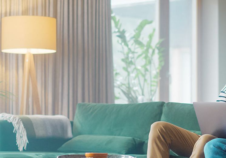 Couple looking at a laptop screen together while sat on a green sofa. 