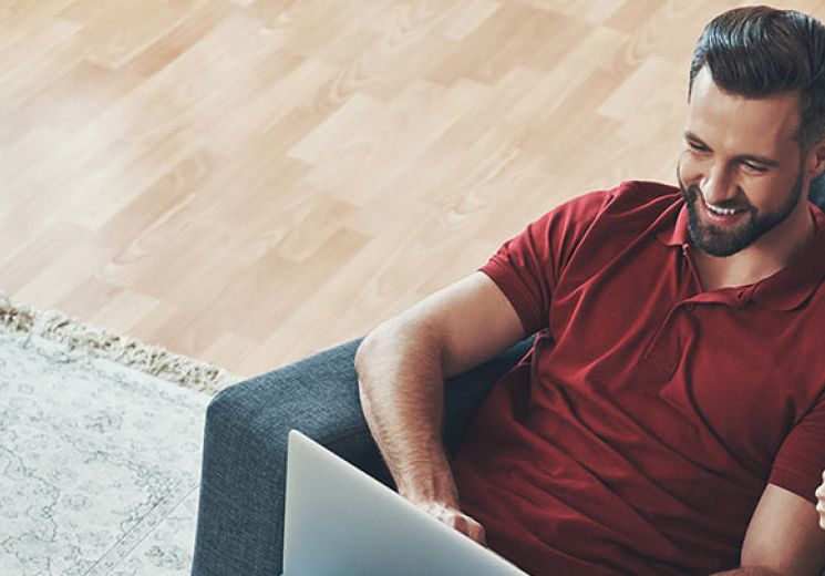 A lady and man sat on a sofa looking at a laptop. 
