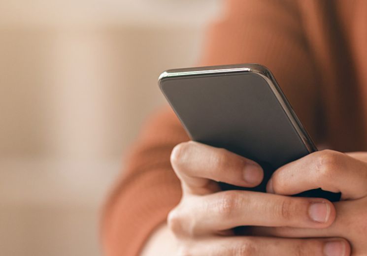 A man in an orange jumper using his phone to switch to paperless. 