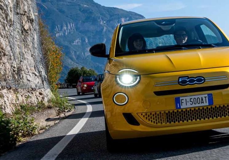Yellow Fiat 500 driving on a coastal road.