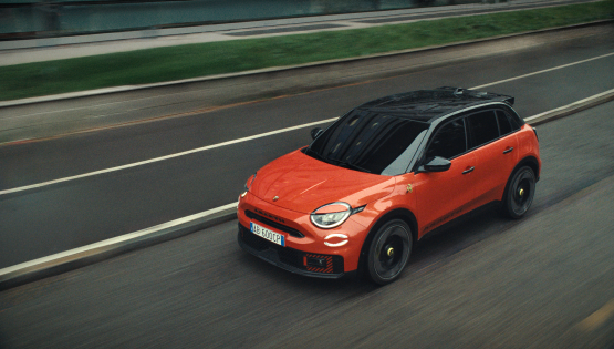 Orange Abarth 600e driving on a road.