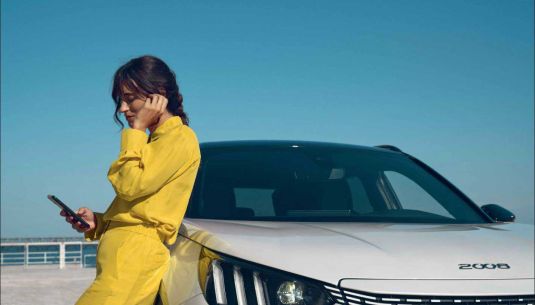 A lady is leaning on a white Peugeot 2008 while on her phone