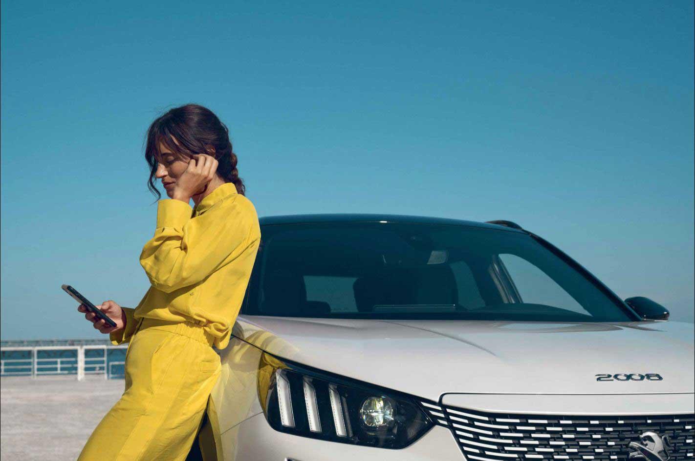 A lady is leaning on a white Peugeot 2008 while on her phone